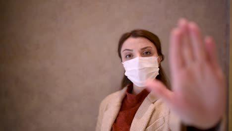 Beautiful-girl-wearing-protective-medical-mask-and-fashionable-clothes-holds-hand-up-as-stop-sign-New-normal-lifestyle-concept