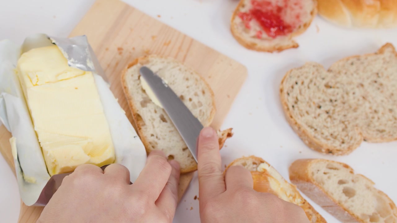 Overhead shot of person slicing butter and spreading it onto fresh sourdough bread slices.
