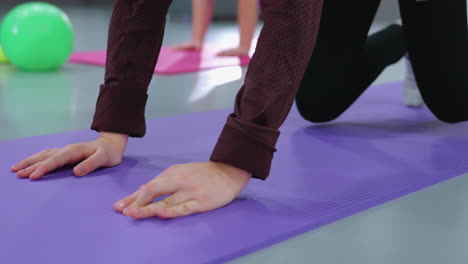 primer plano de ángulo bajo de las manos en una alfombra de gimnasio, mostrando individuos arrastrándose hacia atrás durante una sesión de entrenamiento en grupo, destacando la posición de las manos