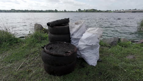 viejos neumáticos usados y sacos de basura en la orilla del lago