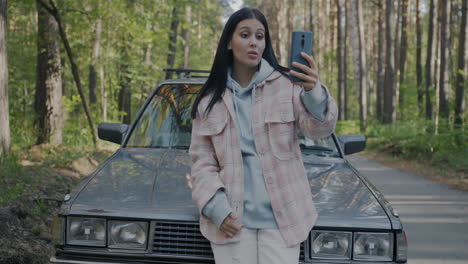 woman taking a selfie by a vintage car in the forest