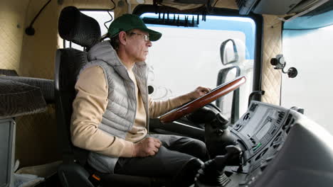 side view of older worker wearing cap and vest driving a truck in a logistics park 3