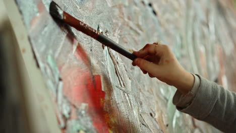 Unrecognizable-painter-hand-making-brush-stroke-on-canvas-in-art-studio.