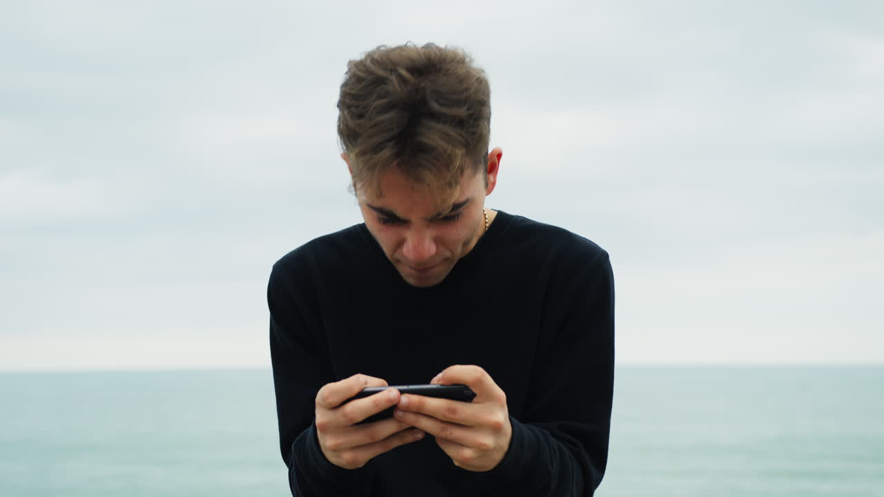 괴짜 소년 은 바다 근처 에서 드폰 으로 게임 을 치고 있다