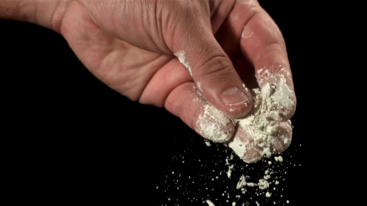 Hvidt pulver falder fra en hånd i slowmotion på sort baggrund