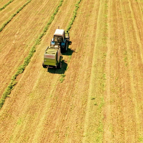 aerial view of the wide yellow field in the countryside. agricultural tractor pressing grass into bale on the natural summer background.