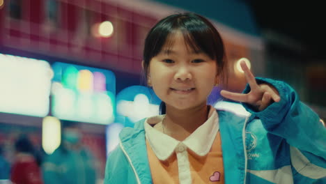 cute female asiatic child kid portrait smiling and v for victory hands sign straight in to camera with bokeh effect