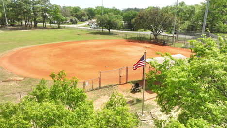 Schwenkende-Amerikanische-Flagge-Vor-Leerem-Baseballfeld-An-Heißen-Sommertagen---Vorwärtsflug-Aus-Der-Luft