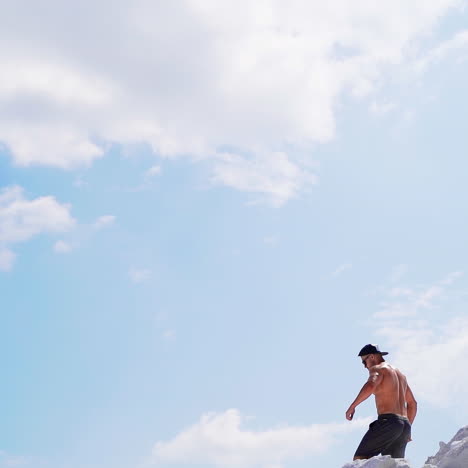 shirtless man going down the hill. back view of muscular sportsman in the mountains under blue sky. view from below. slow motion.