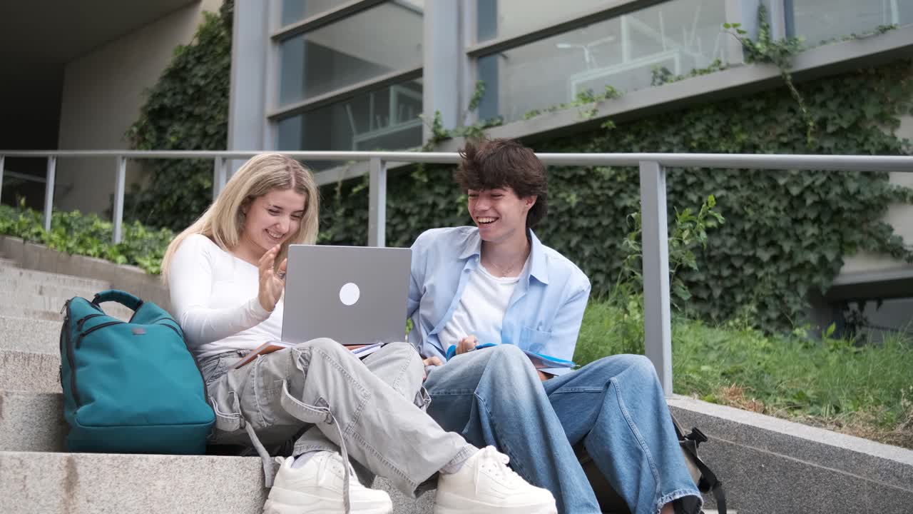 Friends with laptop celebrating exam results on steps of university