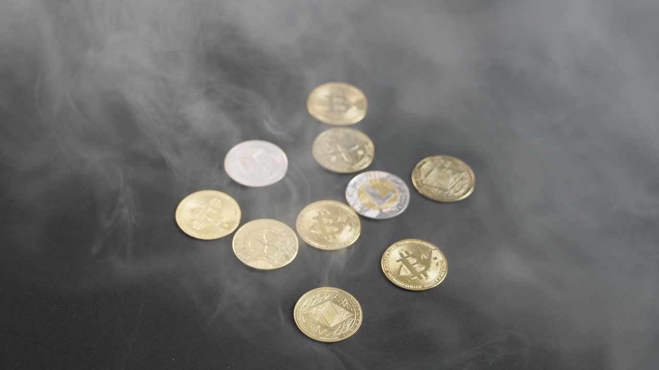 Several cryptocurrency coins, including Bitcoin, Ethereum, Litecoin, Tether, and Neo, on a dark table as smoke pours over and gradually clears