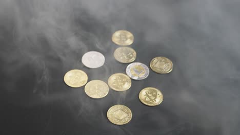 several cryptocurrency coins, including bitcoin, ethereum, litecoin, tether, and neo, on a dark table as smoke pours over and gradually clears