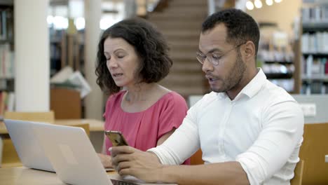 two teachers working at library with digital devices