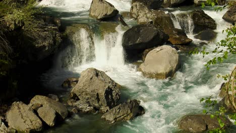 Alpine-mountain-stream-surging-over-boulders-and-rocks,-high-angle-slow-motion