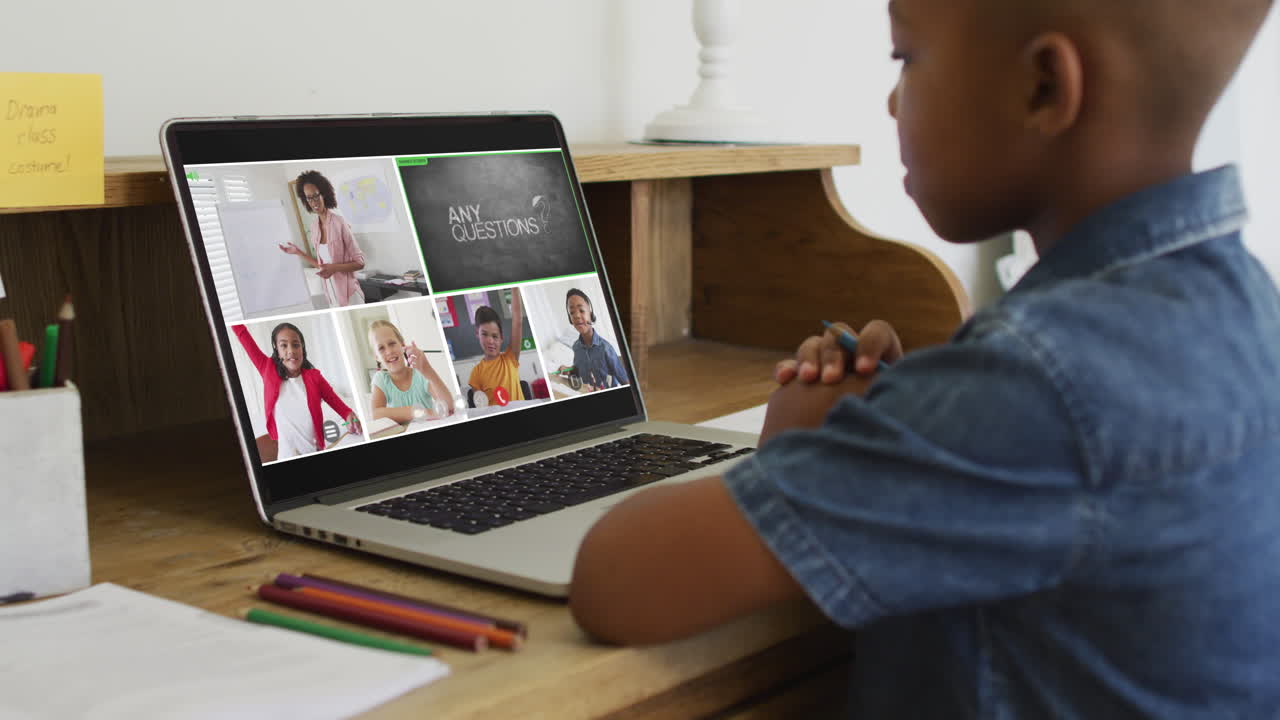 Schoolboy using laptop for online lesson at home, with diverse teacher and class on screen