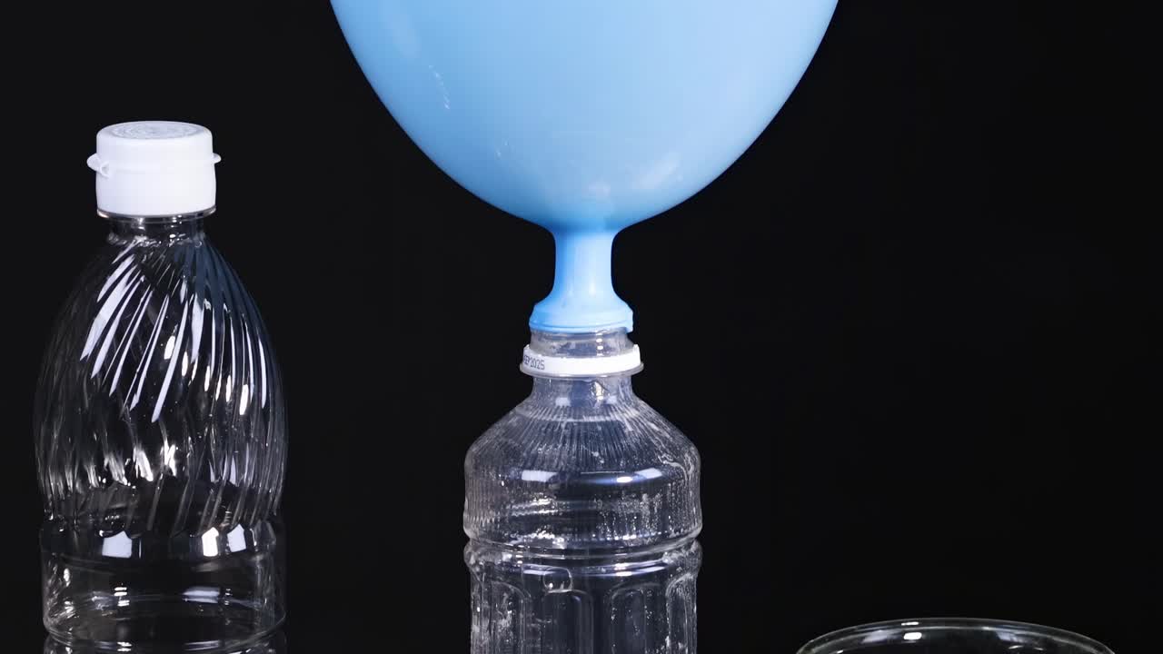 A blue balloon inflates on a bottle using white powder and liquid in a lab setup.