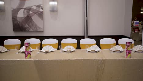 a gorgeous close-up shot captures a long dining table at a wedding with stunning golden and white chairs