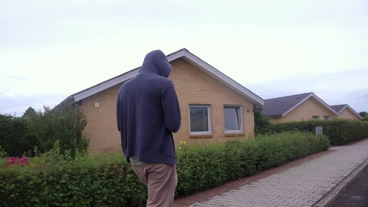 Hooded man walking on a sidewalk.