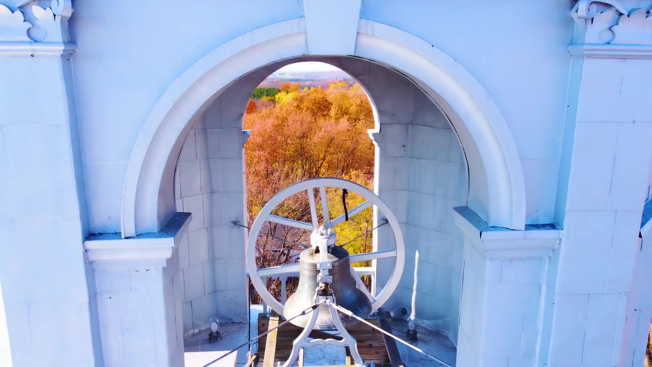 Un campanile storico in un piccolo paese in autunno, circondato da alberi colorati, vista aerea.