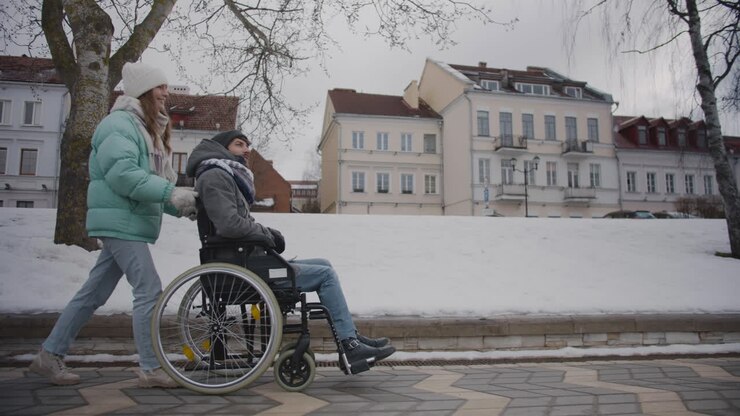 vue latérale d'une femme caucasienne heureuse emmenant son amie handicapée en fauteuil roulant pour une promenade dans la ville d'hiver et parlant ensemble