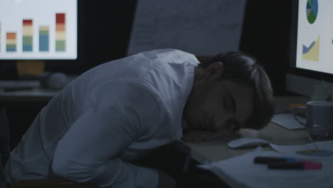 Tired-business-man-sleeping-on-desk-front-computer-screen-in-night-office.