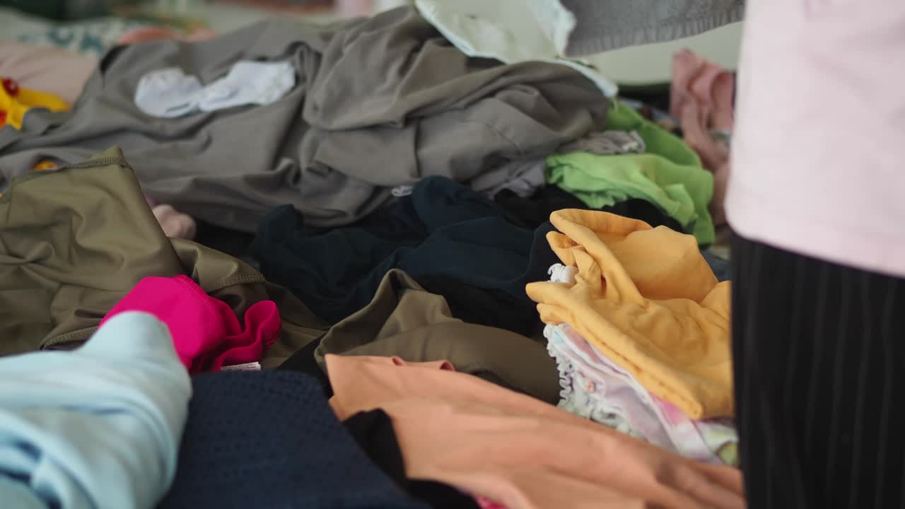 A large pile of clothes, possibly laundry, with a person's hand sorting through it