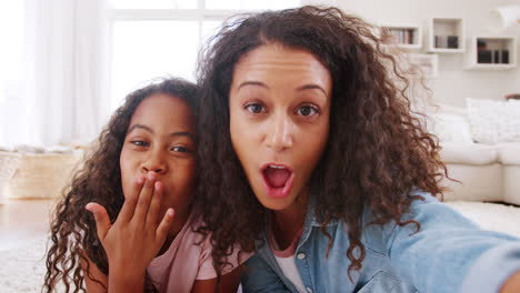 mother and daughter lying on rug and posing for selfie at home