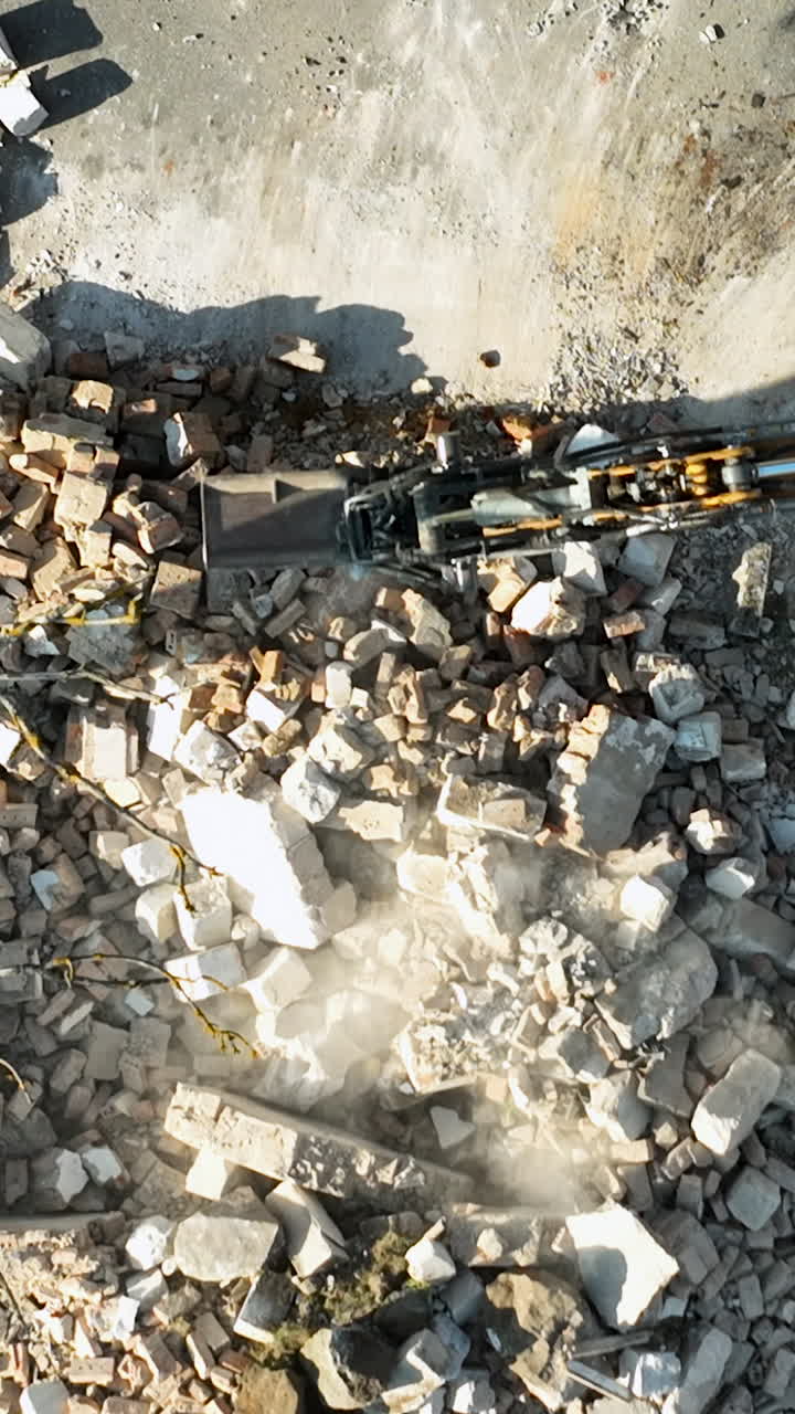 Cinematic aerial top down shot of heavy machinery clearing rubble and demolishing a building structure. Useful for urban development and industrial waste management content