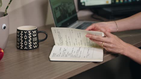 la cámara se mueve hacia los lados como una joven blanca mujer caucásica manos da la vuelta a través de las páginas de un diario de cuaderno lleno de escritura técnica en un entorno de oficina corporativa