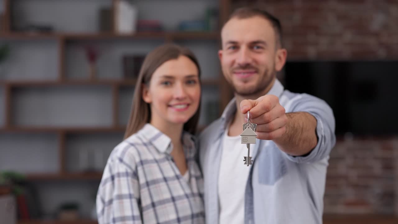 Young couple showing bunch of keys from new house on camera. Happy homeowners on relocation day. Real estate and tenancy concept. Loan mortgage for young family.