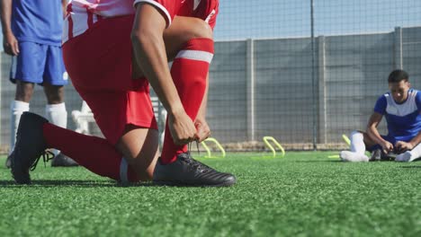 Jugadores-De-Fútbol-Atando-Sus-Zapatos-En-El-Campo