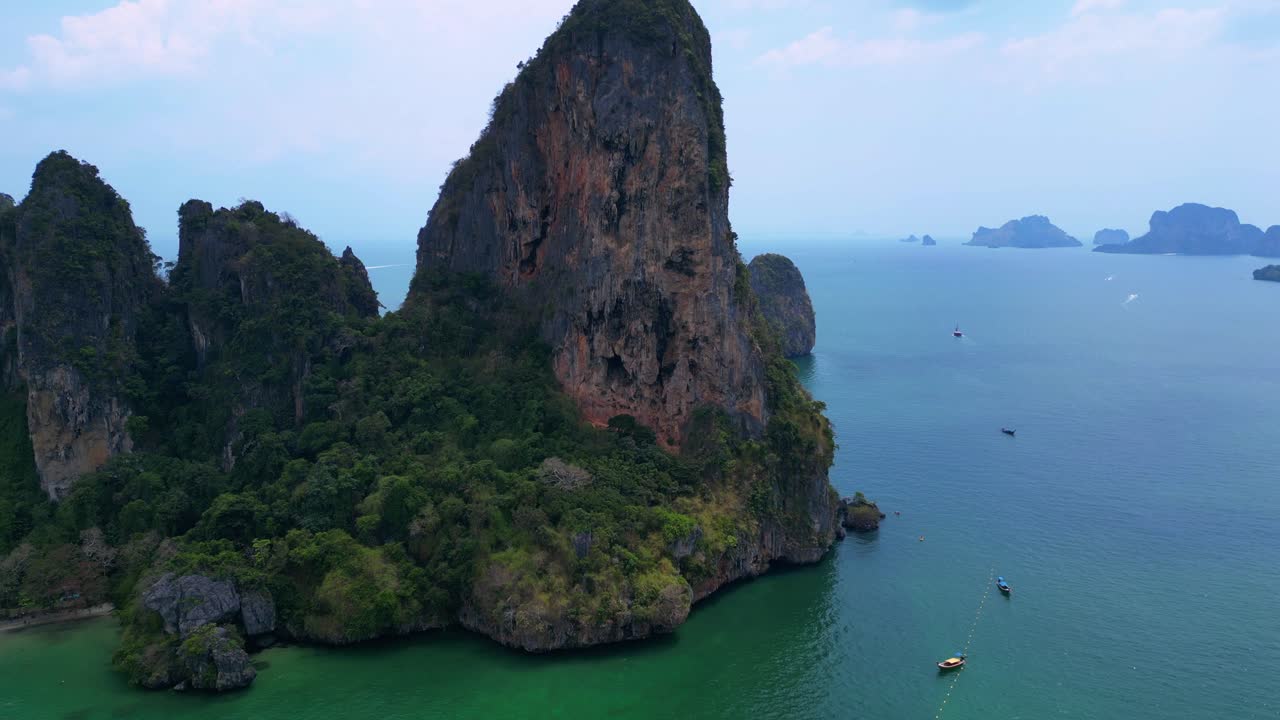 Railay Beach, showcasing its famous limestone cliffs, lush greenery, and the vibrant turquoise waters of the Andaman Sea. static tripod hovering drone