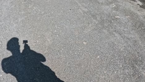 a person's shadow capturing video on pavement.