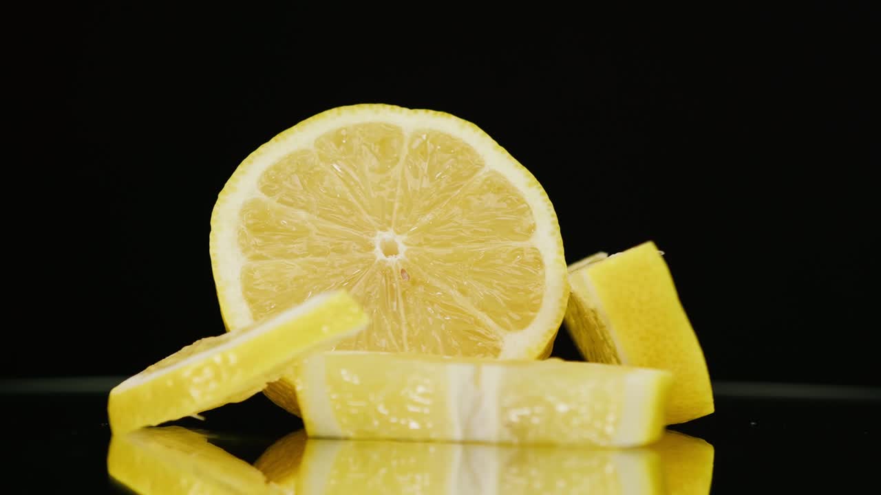 primer plano de piezas de limón maduras giratorias sobre un fondo negro, haciendo un cóctel de cítricos, bebiendo limonada fría, disparando frutas frescas en rodajas