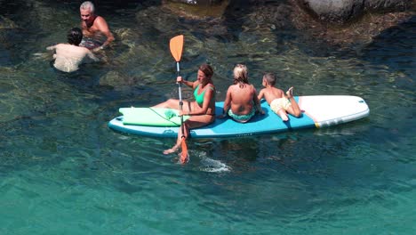 family paddle boarding and swimming in clear waters