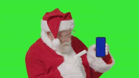 portrait shot of santa holding blue screen mobile phone in front of a green screen