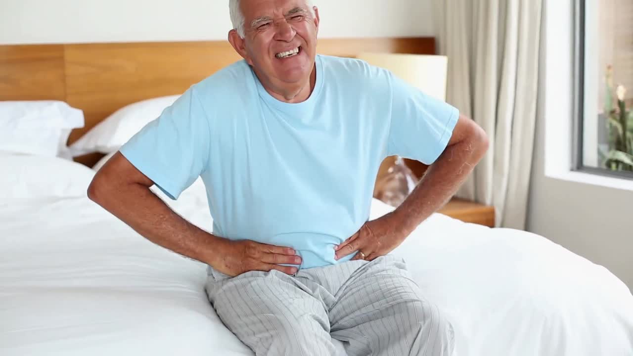 Senior man sitting on bed with a stomach ache