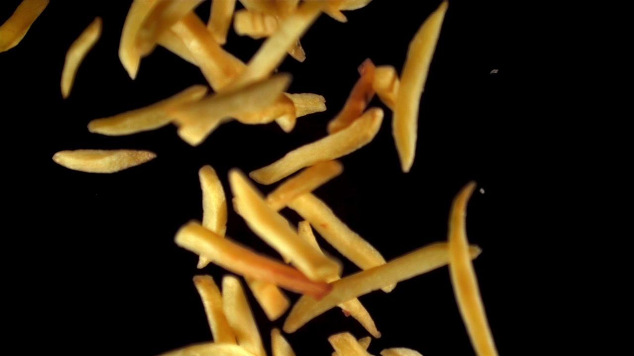 Golden French Fries Falling in Slow Motion on Black Background