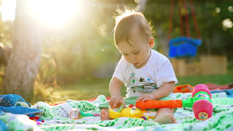 nice cute baby boy plying on the plaid outdoors. beautiful child touching bright toys with interest. bright sun at backdrop.