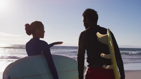 African-american-couple-talking-and-carrying-surfboards-on-the-beach