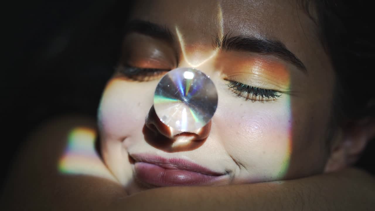 Reclining woman on arm in studio, focused light through prism casting rainbow on eyeshadow, lips