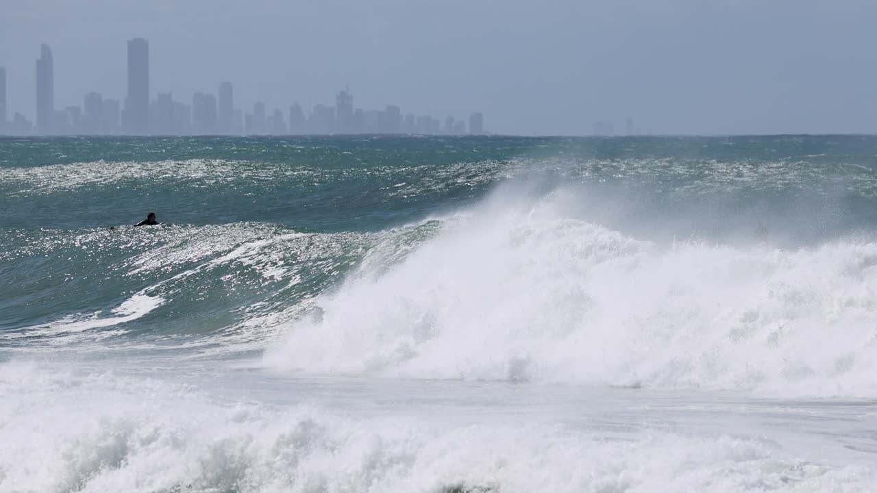 먼 도시의 스카이 라인을 배경으로 큰 바다 파도가 깨지고 있습니다.