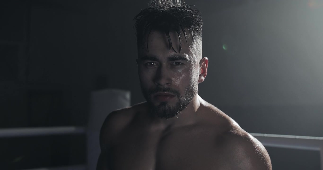 Pugile intenso con i capelli bagnati che fissa la telecamera in un ring buio