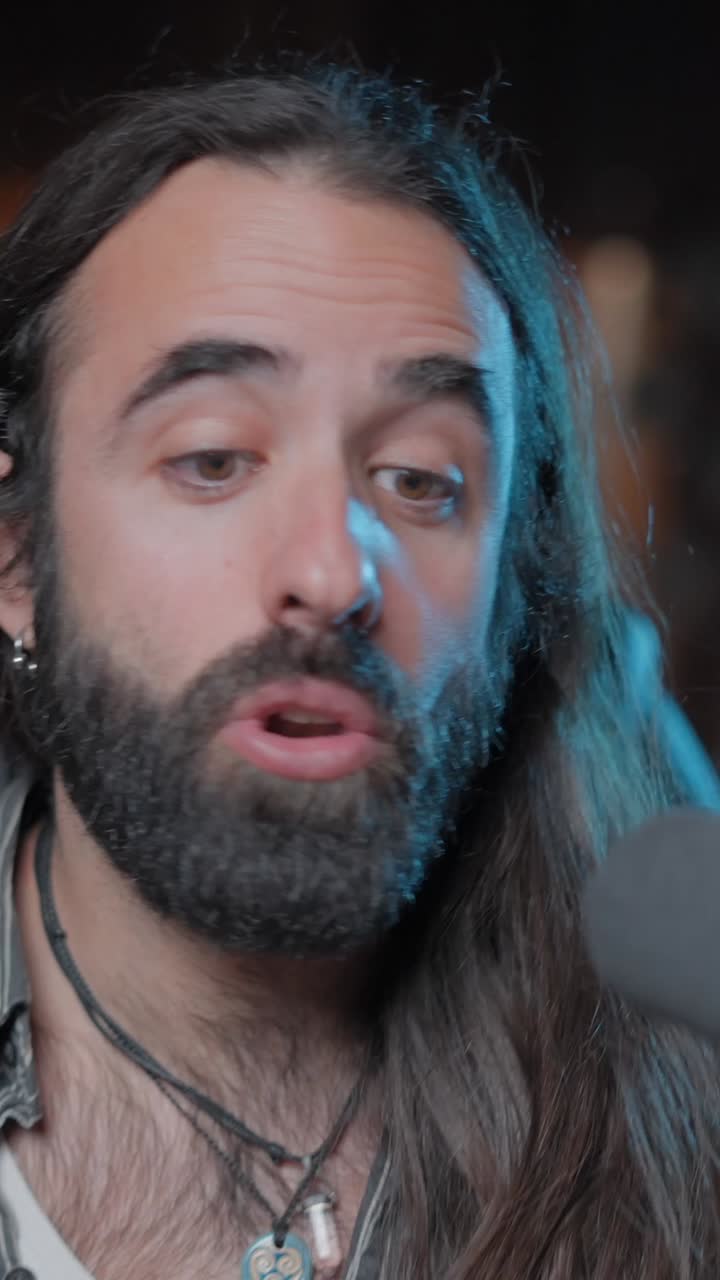 Man with beard and long hair speaking into a microphone while recording a podcast