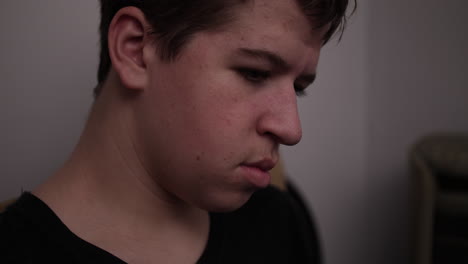 Closeup-of-the-face-and-eyes-of-a-sad,-serious-young-man,-teen-boy-sitting-in-his-bedroom-looking-at-trading-cards