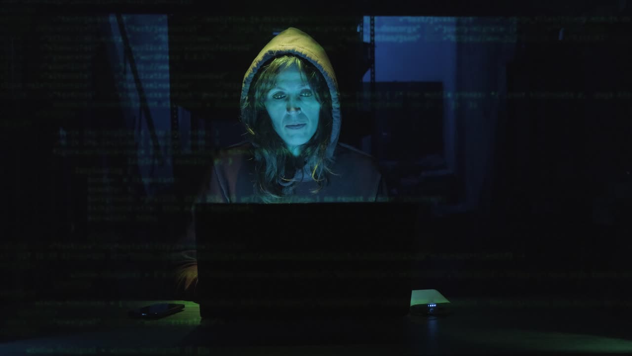 Female Hacker In Hoodie Coding On A Laptop With Overlapping Computer Code. medium shot