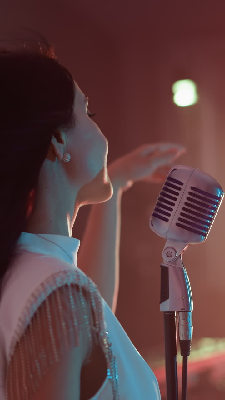 가수가 빈티지 마이크 앞에 서서 손과 몸을 열정적으로 움직이고 있으며, 사이드 글 은 역동적인 에너지와 표현력있는 공연을 따뜻하게 조명된 공간에서 포착합니다.