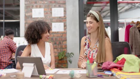 Two-happy-diverse-female-designers-talking-and-shaking-hands-at-fashion-studio,-in-slow-motion