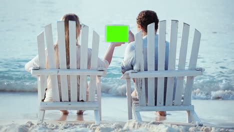 Mujer-Y-Hombre-Sentados-En-La-Playa-Mirando-La-Plataforma-Con-Pantalla-Verde