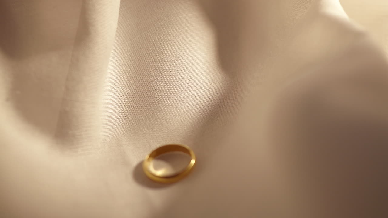 Lasciando scivolare un anello d'oro su un panno color crema, un gioiello prezioso.